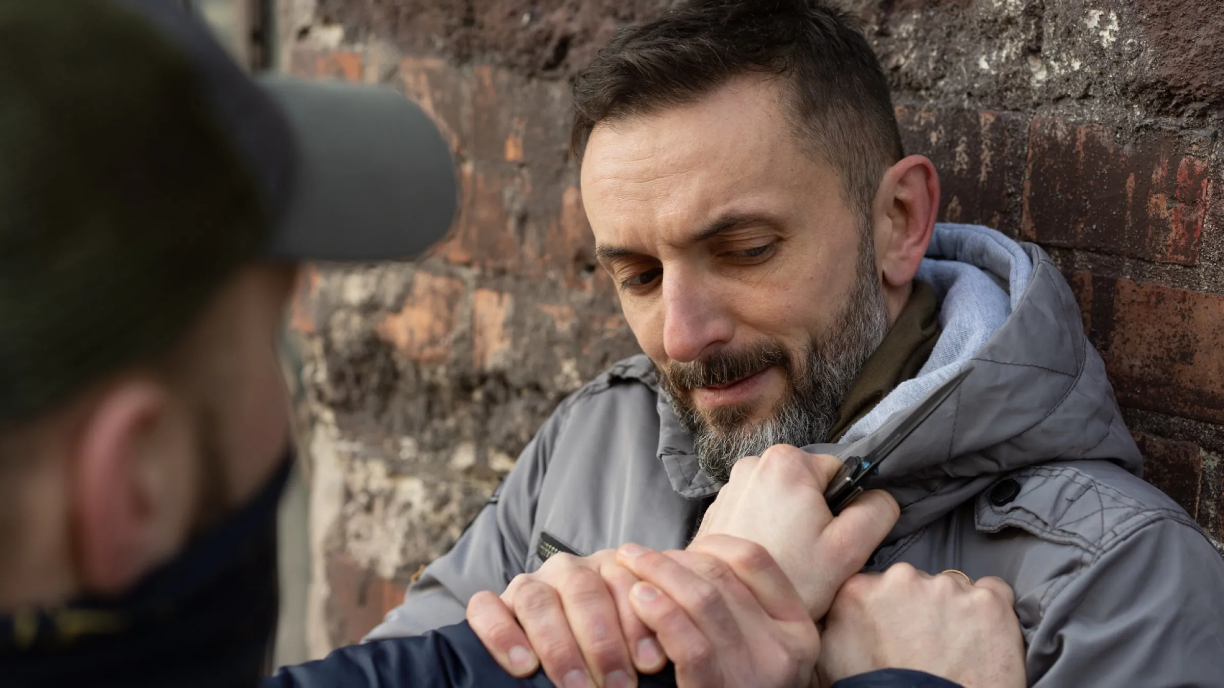 A knife-defence drill close-up — both hands pinning the attacker's blade hand against the body