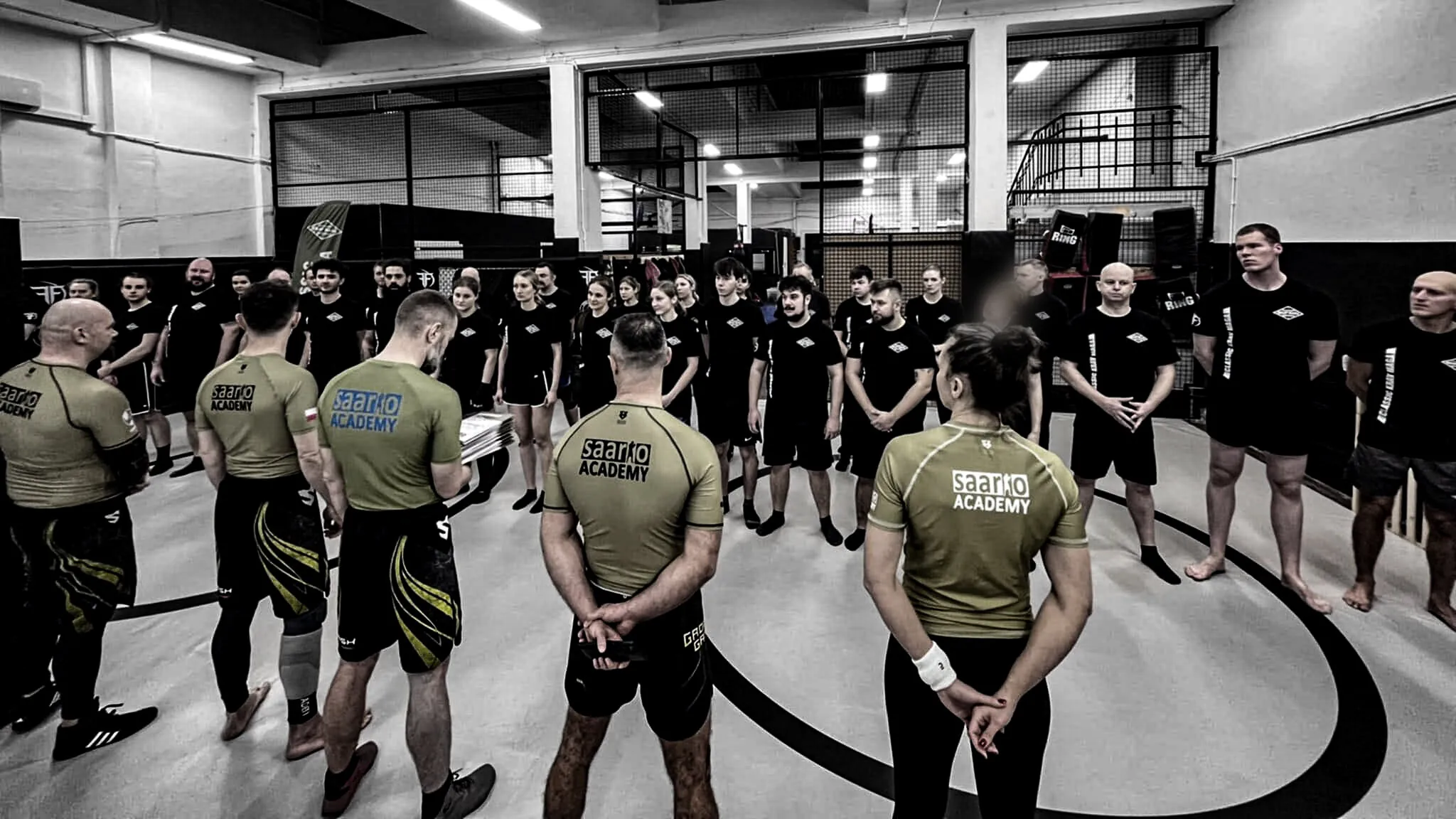 A Saario Academy class circled around an instructor's briefing on the training mat