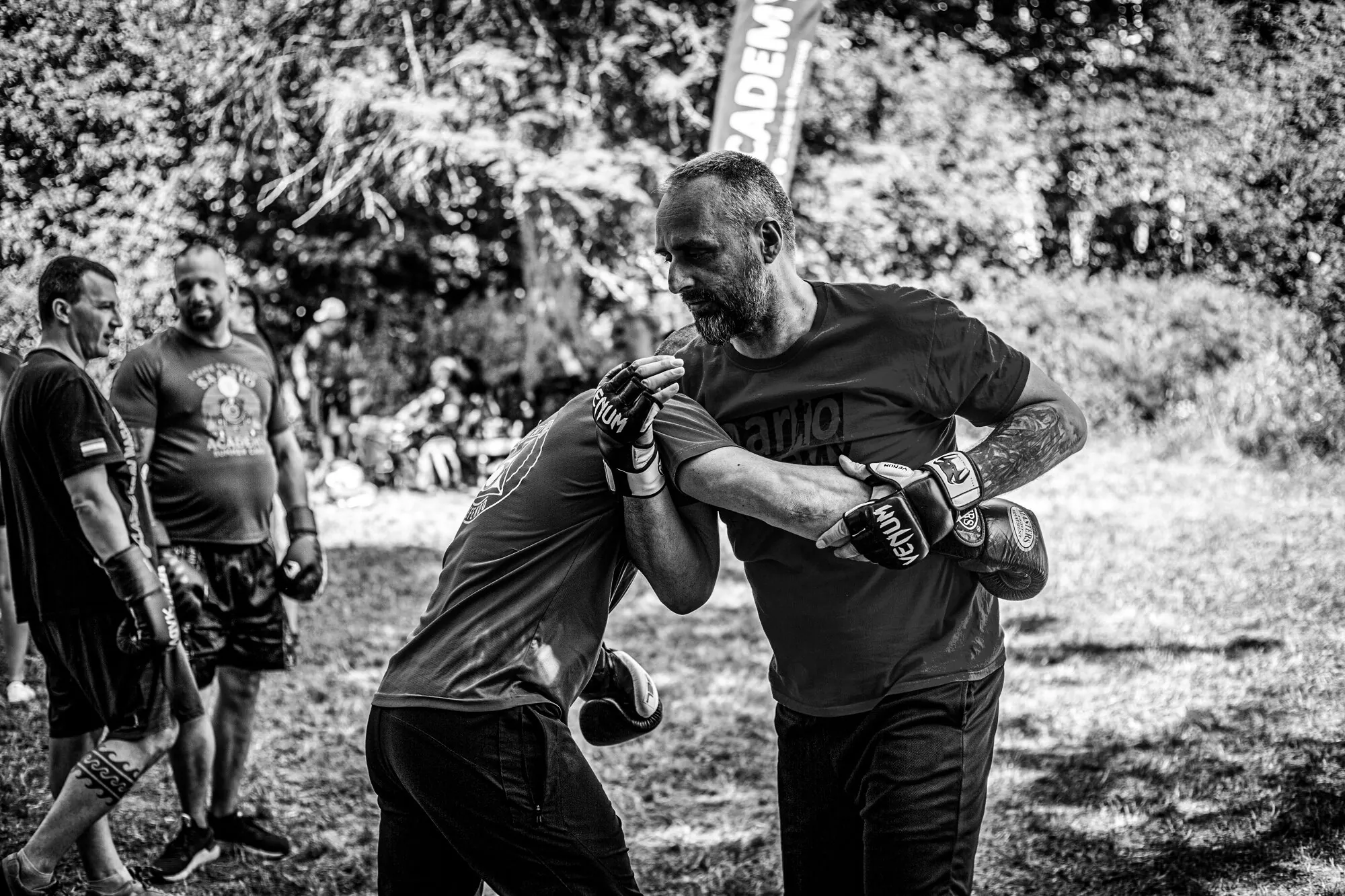 Outdoor summer camp training — an instructor works an arm-control drill while the group trains around him