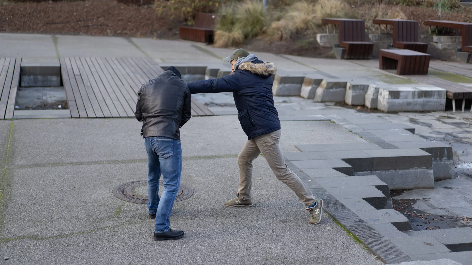 A street-situations training scenario on a Warsaw plaza — one man deflects another's sudden grab, both seen from behind