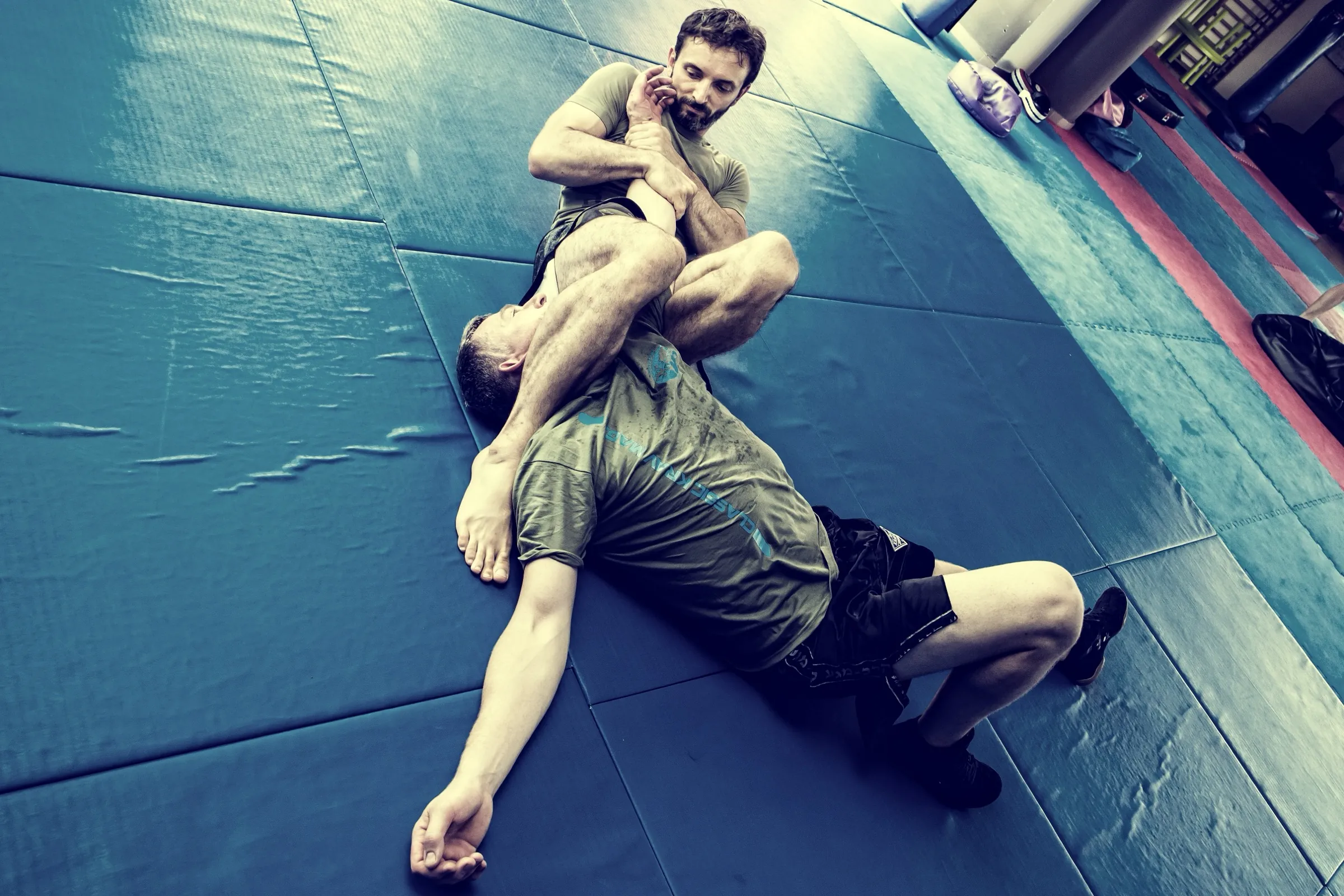 A ground armbar drilled on the mats, cool teal grade, controlled and technical