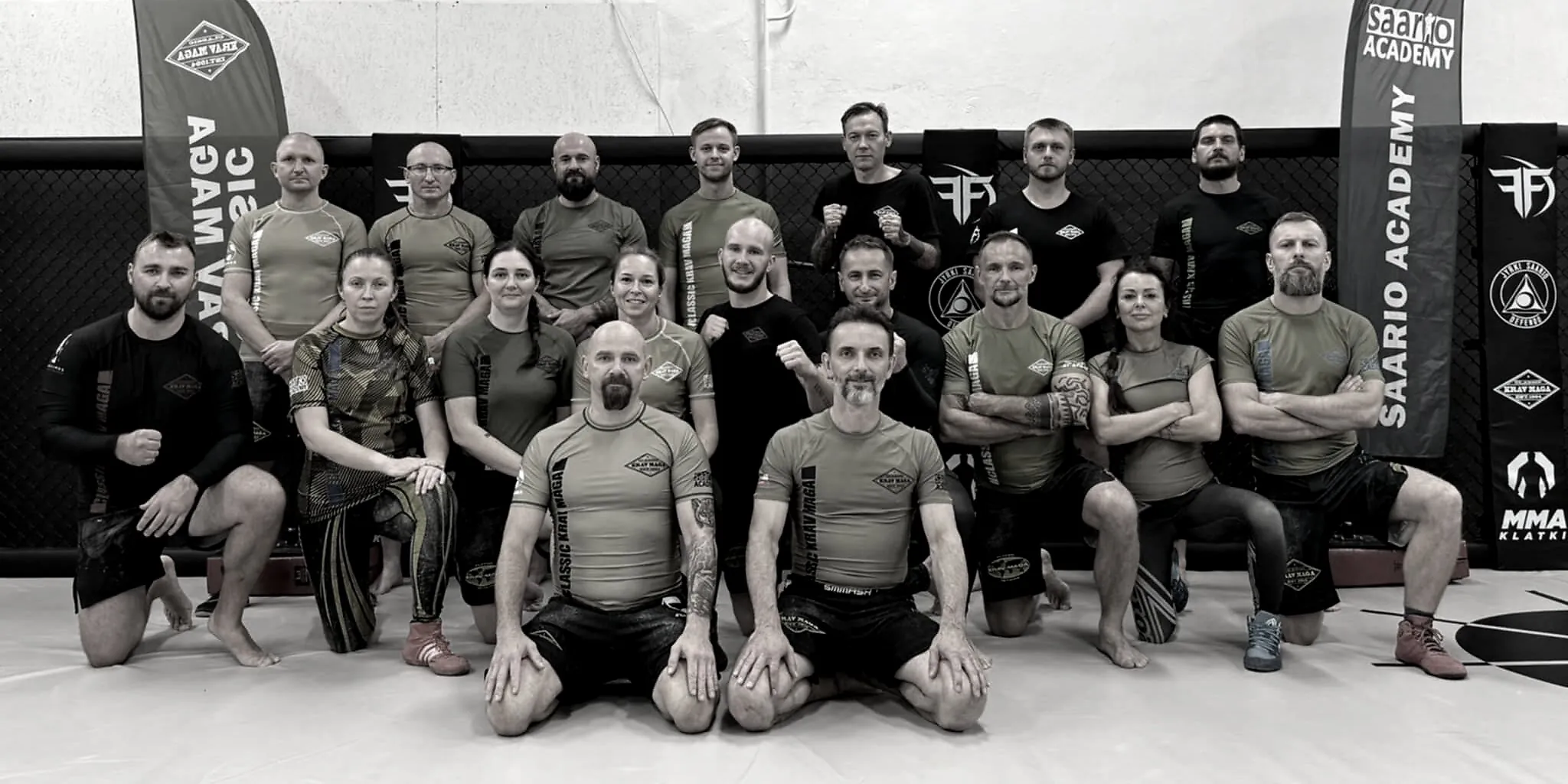 A lined-up group of Saario Academy instructors between Saario Academy banners in a training hall